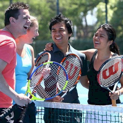 Four people holding rackets, laughing together by a tennis net